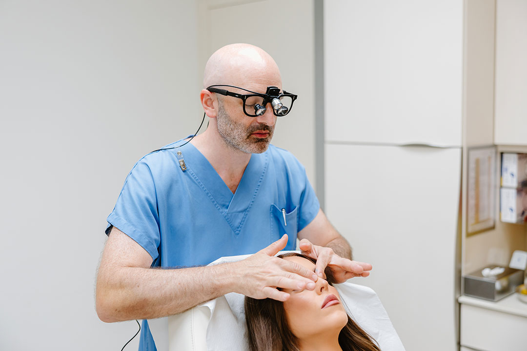Dr. Christoph Grill examining a patient’s nose with surgical loupes – Kuzbari Centre Vienna