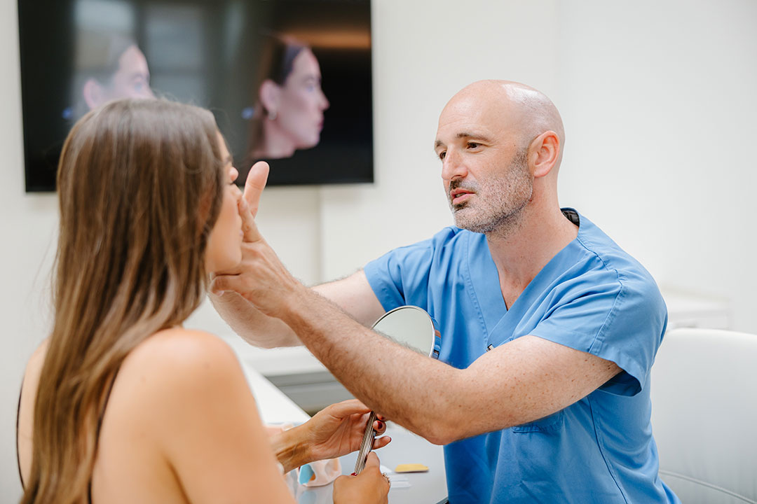Dr. Christoph Grill zeigt einer Patientin im Profil die Oberlider – Kuzbari Zentrum Wien