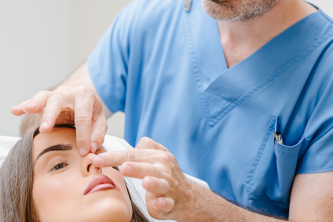 Dr. Christoph Grill tastet Nasenrücken und Nasenspitze einer Patientin ab – Kuzbari Zentrum Wien